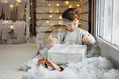 Beaming curlyhair boy opening his christmas gift. New Year lights background Stock Photo