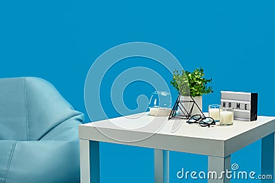 Bean bag, white coffee table with candles on it and in glass candlestick, green flower in pot, glasses, decorative iron Stock Photo