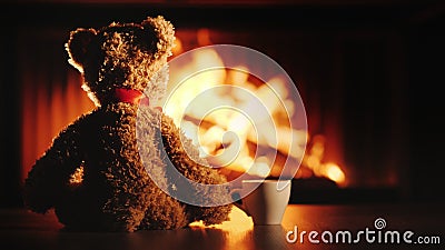 A bear cub with a cup of tea sits opposite the fireplace. Comfort and warmth in the house Stock Photo