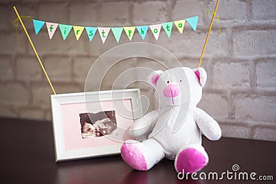 The bear is sitting next to a photo of the baby ultrasound on a brick wall background Stock Photo