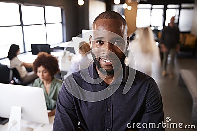 Bearded black male creative standing in a busy casual office, smiling to camera Stock Photo