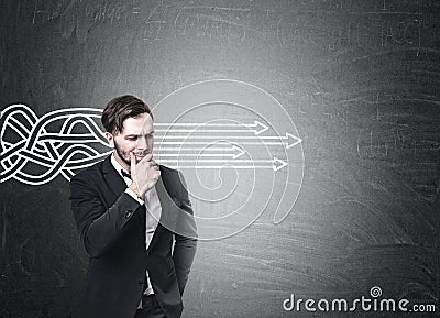 Bearded businessman in a suit is standing near a blackboard with tangled arrows sketch going straight. Stock Photo