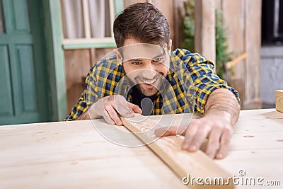 Bearded carpenter measuring wooden plank on table Stock Photo