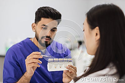 Bearded confident male dentist checking and selecting color of young woman teeth Stock Photo