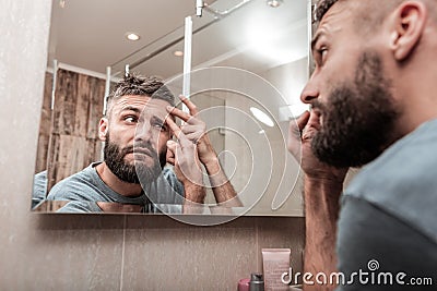 Bearded dark-haired man looking at acne on his face Stock Photo