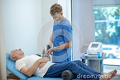 Bearded doctor performing ultrasound elbow treatment on mature patient Stock Photo