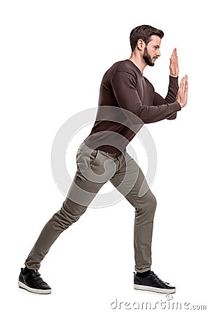 A bearded fit man in casual pants presses his hands over an invisible object in order to move it. Stock Photo
