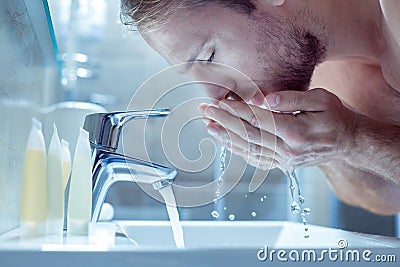 Bearded handsome man washing his face in the morning in light bathroom Stock Photo