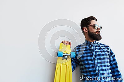 Bearded hipster in checkered shirt holding yellow skateboard Stock Photo