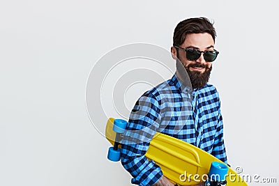 Bearded hipster in checkered shirt holding yellow skateboard Stock Photo
