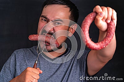 A bearded hungry man greedily eats a huge piece of sausage impaled on a fork, the concept of disruption from dietary nutrition Stock Photo