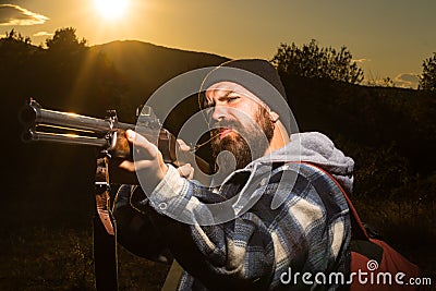 Bearded hunter man holding gun and walking in forest. Rifle Hunter Silhouetted in Beautiful Sunset. Autunm hunting Stock Photo
