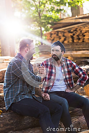bearded lumberjacks shaking hands of each other and sitting on logs Stock Photo