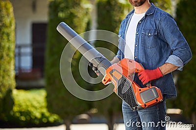Bearded male gardener in gloves holding powerful cordless leaf blower outdoors. Stock Photo