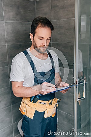 Bearded male plumber making notes in clipboard while checking shower Stock Photo