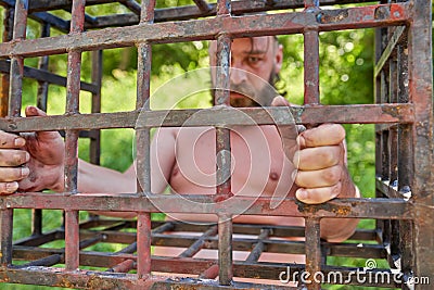 Bearded man behind iron bars, focus on fingers gripping steel bars Stock Photo