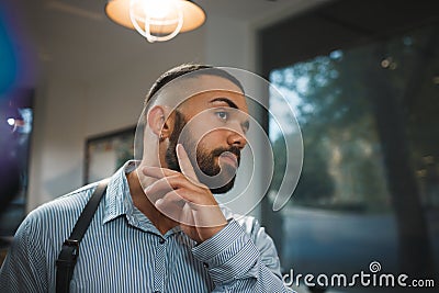 Bearded man on a blurred background. Handsome man touching new beard in a barbershop. Hipster style concept. Copy space. Stock Photo