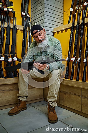 Bearded man choosing automatic rifle in gun store Stock Photo