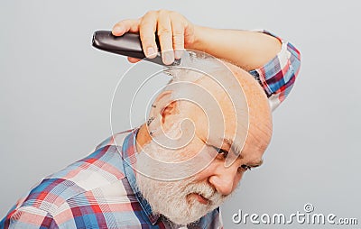 Bearded man cutting his own hair with a clipper. Man hair treatment. Gray man hair clippings. Bald man hairclipper Stock Photo