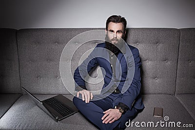 Bearded man dressed in suit and with laptop browsing internet; Stock Photo