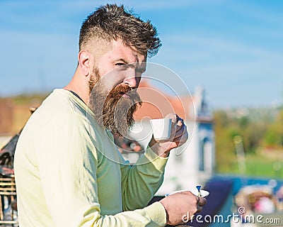 Bearded man with espresso mug, drinks coffee. Man with beard and mustache on strict face drinks coffee, urban background Stock Photo