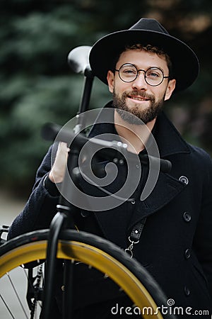 Bearded man with a fixie bicycle. Low angle view of confident young bearded man carrying his bicycle on shoulder and looking at Stock Photo