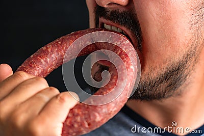 A bearded man greedily bites a round sausage. Hunger and gluttony Stock Photo