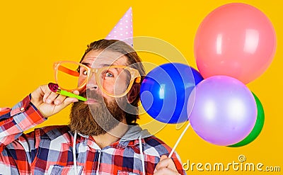 Bearded man in party hat and glasses with balloons blowing noisemaker. Birthday holiday celebration. Stock Photo