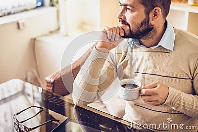 Bearded man sitting with cup of morning coffee and looking out the window Stock Photo