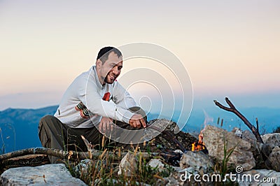 Bearded man sitting near fireplace on top of mountain Stock Photo