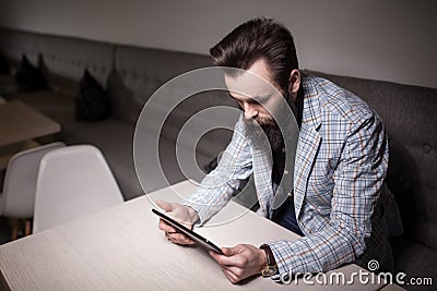 Bearded man in suit and with tablet sitting in cafe and browsing Stock Photo