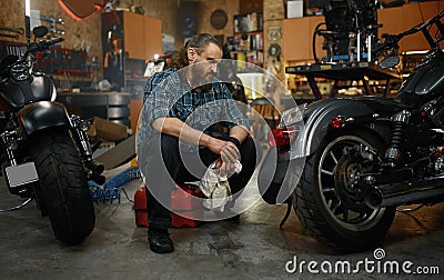 Bearded mature man biker cleaning motorcycle in garage workstation Stock Photo