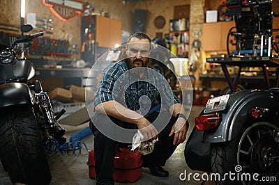 Bearded mature man biker cleaning motorcycle in garage workstation Stock Photo