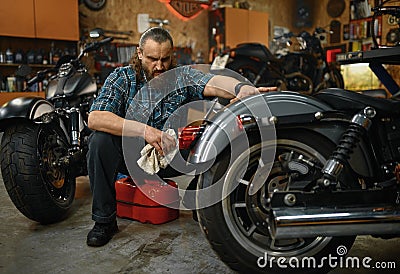 Bearded mature man biker cleaning motorcycle in garage workstation Stock Photo