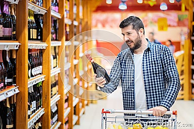 Bearded mature man in supermarket choosing red wine bottle from shelves Stock Photo