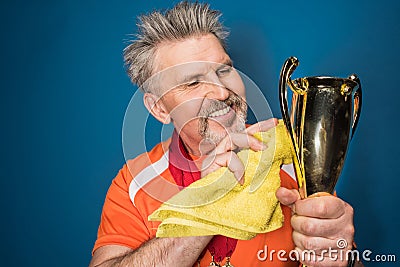 Bearded mature sportsman cleaning trophy cup Stock Photo