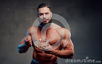 Bearded bodybuilder eating his diet in gray background Stock Photo