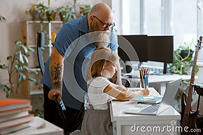 Bearded plump father stands looking at little girl doing hometask at home Stock Photo