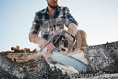 Bearded professional lumberjack wprker wearing plaid shirt using chainsaw for work on sawmill Stock Photo