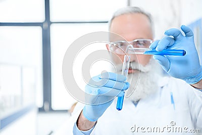 Bearded scientist in protective goggles and gloves holding test tubes with reagents and making experiment Stock Photo