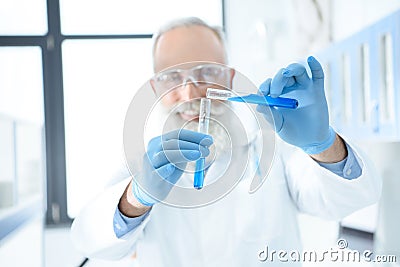 Bearded scientist in protective goggles and gloves holding test tubes with reagents and making experiment Stock Photo