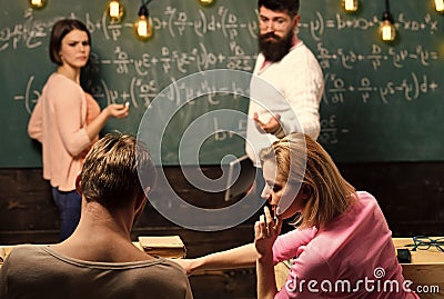 Bearded teacher, lecturer, professor watching students during test, exam, lesson. Students, group mates speaking, asking Stock Photo