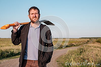 A bearded white impudent-looking man with a shovel on his shoulder in a black jacket Stock Photo