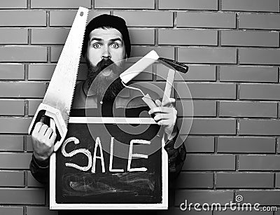 Bearded worker holding various building tools and board, surprised face Stock Photo