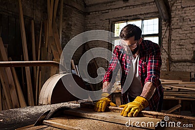 bearded worker in protective googles and gloves using machine saw Stock Photo