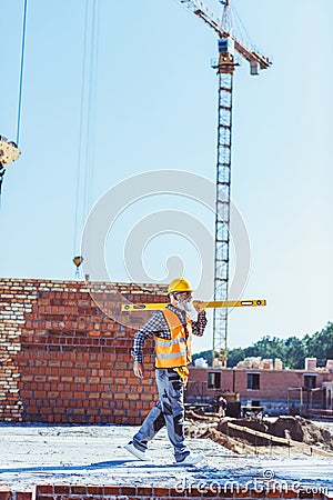 Bearded worker in reflective vest and hardhat walking with spirit level across Stock Photo