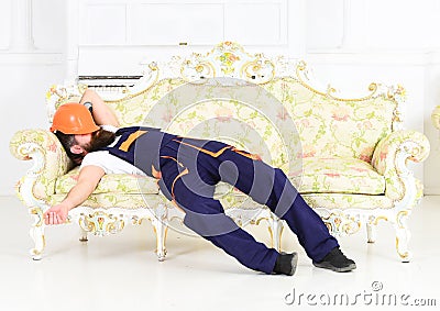 Bearded worker sleeping on vintage sofa with protective helmet over his face. Tired builder enjoying break and having Stock Photo