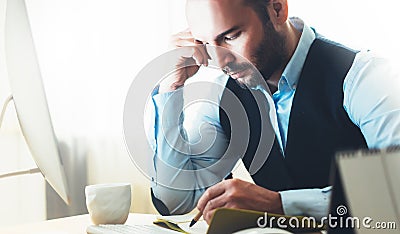 Bearded young businessman working on modern office. Consultant man thinking looking in monitor computer. Manager writes in noteboo Stock Photo