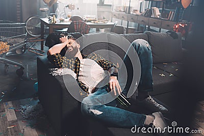 Bearded young man with bottle lying on sofa after party Stock Photo