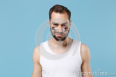 Bearded young man 20s years old in white shirt, smear clay facial mask on cheek isolated on blue pastel background Stock Photo
